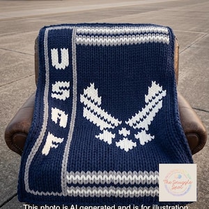 May include: A navy blue knitted blanket with white and gray accents, featuring the letters "USAF" and the Air Force emblem. The blanket is draped over a brown leather chair, with military aircraft in the background.