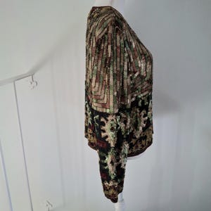 Puede incluir: Top de manga larga con lentejuelas con un patr&oacute;n geom&eacute;trico en tonos marr&oacute;n, verde y dorado. La parte inferior del top presenta un fondo negro con un dise&ntilde;o floral. El top se exhibe en un maniqu&iacute; blanco.