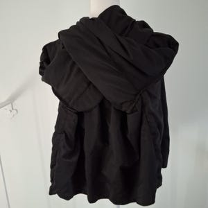 Puede incluir: Chaqueta negra con capucha exhibida en un maniqu&iacute;. La chaqueta tiene una capucha grande y un dise&ntilde;o suelto y fluido. La tela parece ser un material ligero, adecuado para usar en capas. La chaqueta es de color negro liso.