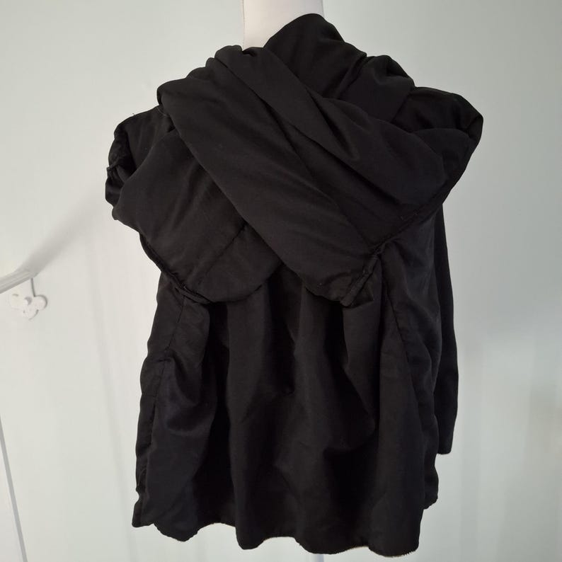 Puede incluir: Chaqueta negra con capucha exhibida en un maniqu&iacute;. La chaqueta tiene una capucha grande y un dise&ntilde;o suelto y fluido. La tela parece ser un material ligero, adecuado para usar en capas. La chaqueta es de color negro liso.