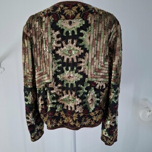 Puede incluir: Una chaqueta negra con intrincados detalles de lentejuelas. La chaqueta presenta un patr&oacute;n geom&eacute;trico en tonos verdes, dorados y marrones. Las lentejuelas crean un efecto texturizado y brillante, agregando un toque de glamour a la prenda.