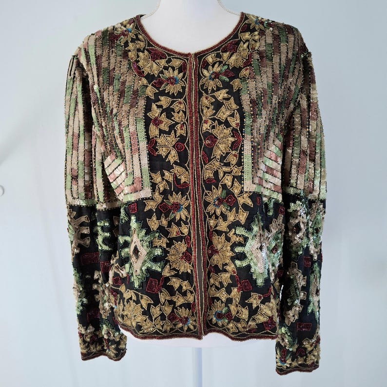 Puede incluir: Chaqueta totalmente con lentejuelas con cuello redondo y mangas largas. La chaqueta presenta una base negra con estampados florales y geom&eacute;tricos en dorado, rojo y verde. Las mangas y la parte superior del cuerpo tienen rayas verticales en tonos marrones, verdes y dorados.