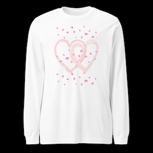 May include: White long-sleeve shirt featuring a watercolor design of two intertwined pink hearts and scattered pink petals. The shirt has a crew neck and long sleeves, perfect for casual wear.