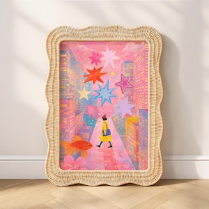 May include: A framed art print featuring a whimsical cityscape scene. The artwork depicts a person in a yellow coat walking down a street lined with buildings, with colorful stars overhead and a goldfish in the foreground. The frame is made of woven wicker.