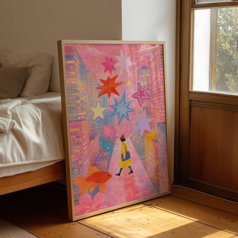 May include: A framed art print featuring a whimsical cityscape scene. The artwork depicts a person in a yellow coat walking down a street, with a goldfish and colorful stars. The buildings are pink and yellow, creating a vibrant and dreamlike atmosphere.