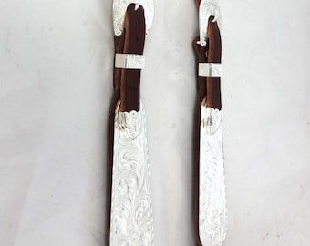 Puede incluir: Un cabezada de cuero marrón para caballo con conchos y hebillas plateadas. Los conchos están grabados con diseños florales.