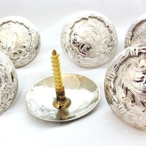 Könnte beinhalten: Sechs silberfarbene Metall-Conchos mit floralem Design und einer Messing-Schraube. Die Conchos sind rund und haben ein erhabenes Design.