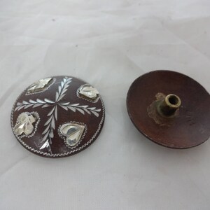 May include: Two round, brown, wooden buttons with silver leaf designs. One button has a small, brass, round knob on the back.