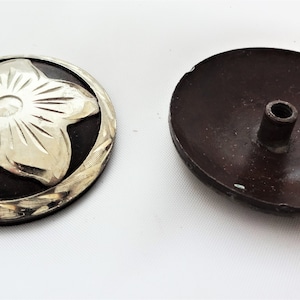 Op de afbeelding: Een zilveren en zwarte metalen knoop met een bloemdessin. De knoop heeft een reliëf bloemdessin met een middelste cirkel en vijf bloemblaadjes. De knoop is rond en heeft een glad oppervlak.