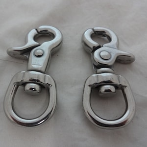 May include: Two silver metal swivel snap hooks with a D-ring on each. The hooks are closed and ready to be attached to a leash or other item.