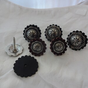 Puede incluir: Conjunto de siete conchos de cuero negro y plateado con un dise&ntilde;o floral decorativo. Los conchos se utilizan para decorar sillas de montar, cinturones y otros art&iacute;culos de cuero.