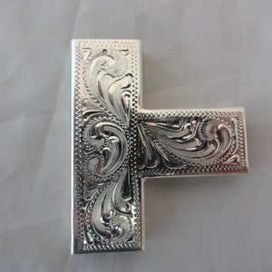 以下が含まれることがあります： 複雑な花の模様が施された、銀色の金属製のT字型の装飾品