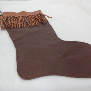 May include: A brown leather stocking with a fringe trim at the top. The stocking has a loop at the top for hanging.