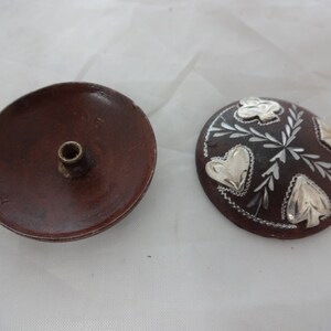 May include: Two wooden decorative items. One is a round dish with a small hole in the center. The other is a round disc with a brown background and silver leaf designs.