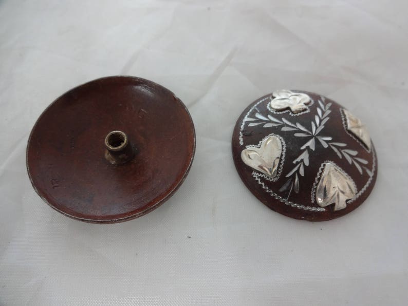 May include: Two wooden decorative items. One is a round dish with a small hole in the center. The other is a round disc with a brown background and silver leaf designs.
