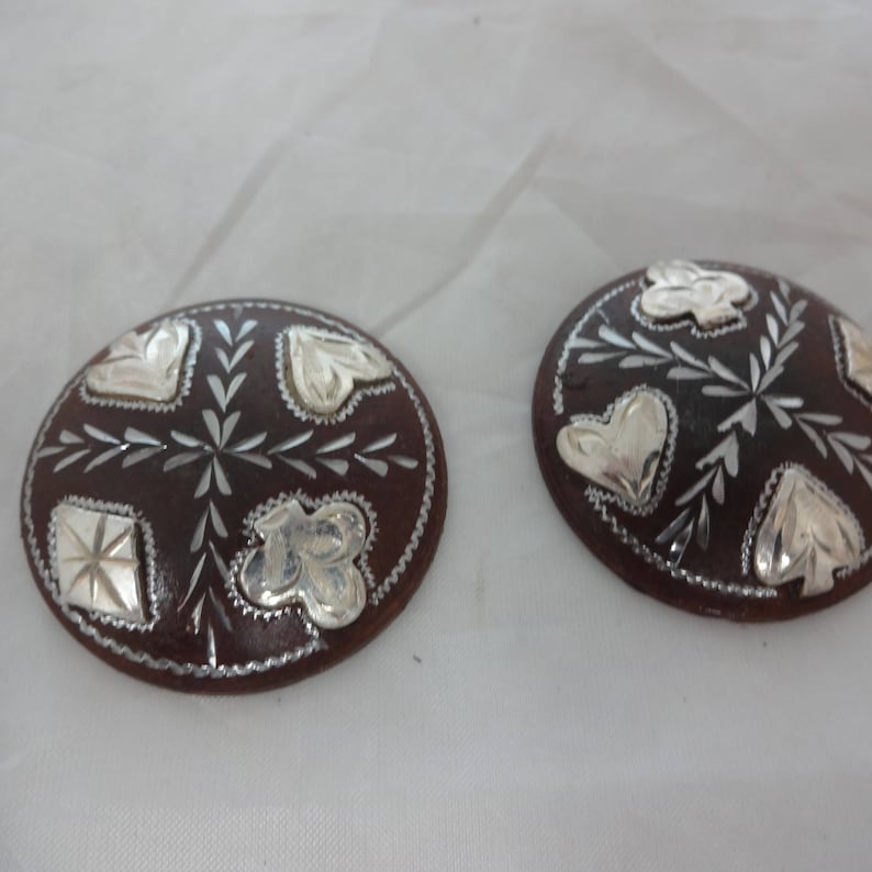 May include: Two brown leather round buttons with silver floral and heart designs.