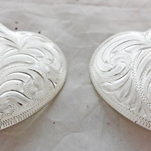 May include: Two silver heart-shaped belt buckles with an intricate floral design.