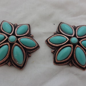 May include: Two copper-toned metal flower-shaped embellishments with turquoise stones. Each embellishment has a central turquoise stone surrounded by six oval-shaped turquoise stones.