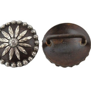Puede incluir: Un par de conchos de metal plateado y marrón con un diseño floral. Un concho tiene un asa de bucle en la parte posterior.