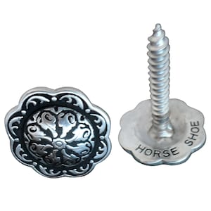 May include: Two silver-toned metal horse shoe tacks with a decorative floral design. One tack has a screw and the other has a flat back. The screw tack has the words "Horse Shoe" engraved on the back.