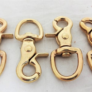 Puede incluir: Cuatro mosquetones giratorios de metal dorado. Cada mosquetón tiene un anillo en D en un extremo y un cierre de resorte en el otro.