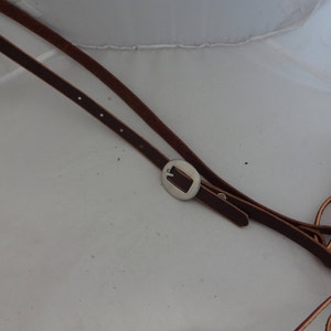 Puede incluir: Dos correas de cuero marrón con una hebilla plateada. Las correas están atadas en un nudo.