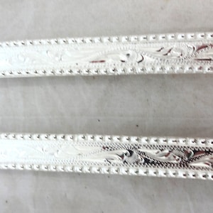 Puede incluir: Dos hebillas de cinturón plateadas con un intrincado diseño floral. Las hebillas son rectangulares y tienen un acabado liso y pulido.