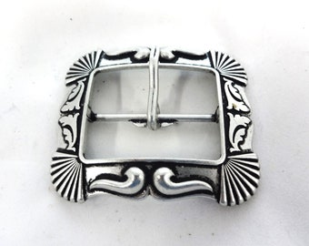 Könnte beinhalten: Silberfarbener Metallschnalle mit einem verzierten Design, das einen rechteckigen Rahmen mit komplizierten floralen und fächerförmigen Details aufweist.