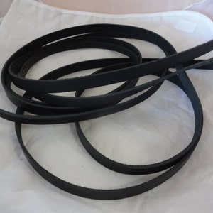 Puede incluir: Primer plano de un conjunto de correas de cuero negro. Las correas tienen aproximadamente 1,2 cm de ancho y están enrolladas juntas.