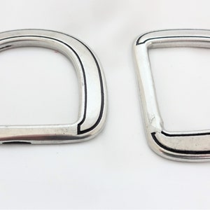 Op de afbeelding: Twee zilveren D-ringen met zwarte afwerking. De ringen zijn glad en hebben een gepolijste afwerking.