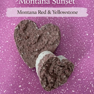 May include: Two heart-shaped, textured, reddish-brown stones on a speckled purple background. The text "Montana Sunset" and "Montana Red & Yellowstone" are displayed above the stones.