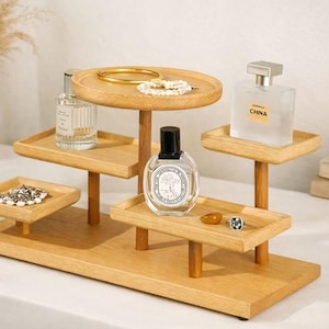 May include: A multi-tiered wooden display stand with various items. The stand holds perfume bottles, jewelry, and decorative items. The stand is made of light-colored wood and has a rectangular base with multiple platforms.