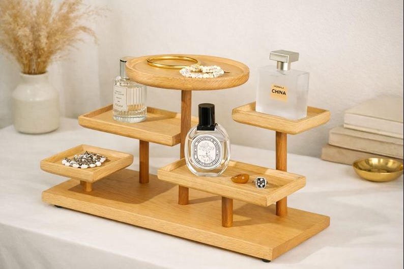May include: A multi-tiered wooden display stand with various items. The stand holds perfume bottles, jewelry, and decorative items. The stand is made of light-colored wood and has a rectangular base with multiple platforms.