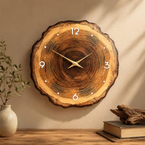 May include: A round wall clock crafted from a natural wood slice featuring visible dark brown tree rings. The clock face displays white numerals at the 12, 3, 6, and 9 o'clock positions, with small white dots for other markers and thin gold-colored hands.