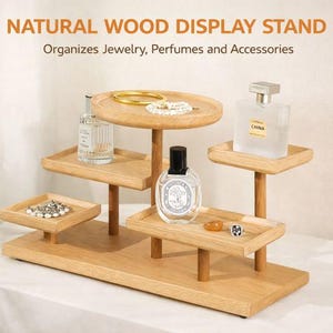 May include: A natural wood display stand with multiple tiers, holding jewelry, perfumes, and accessories. The stand features a rectangular base and several small, square and round trays supported by wooden posts. The text "NATURAL WOOD DISPLAY STAND" is visible.