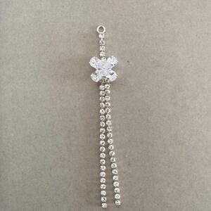 May include: A silver earring component with a floral crystal cluster and two strands of dangling clear crystals. The component has a small loop at the top for attachment. The earring component is approximately 5 cm long.