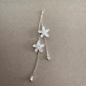 May include: A silver-toned floral pendant with two flower-shaped crystal accents. The pendant features a delicate chain and dangling accents, perfect for adding a touch of elegance to any outfit.