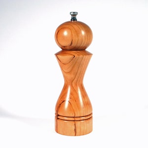 Puede incluir: Un molinillo de sal y pimienta de madera con un acabado de madera natural. El molinillo tiene una parte superior redonda y una base bulbosa.