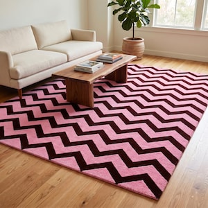 May include: A pink and brown chevron patterned rug. The rug is rectangular and covers a wooden floor. A light-coloured sofa and a wooden coffee table are in the background.