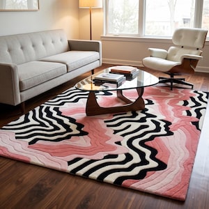 May include: A modern area rug with a unique design. The rug features a pattern of black and white zebra stripes, and shades of pink. The rug is placed in a living room with a sofa, chair, and coffee table.