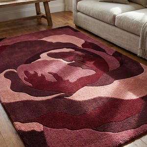 May include: A large, plush area rug with a floral design in shades of burgundy, rose, and mauve. The rug's pattern resembles a stylized rose, adding a touch of elegance to the room. The rug is placed on a hardwood floor.