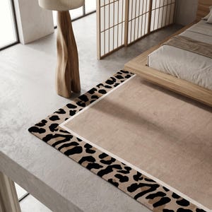 May include: A rectangular area rug featuring a solid beige center panel bordered by a wide frame with a black and brown leopard print pattern. The rug is defined by a thin white line separating the central beige section from the animal print border.