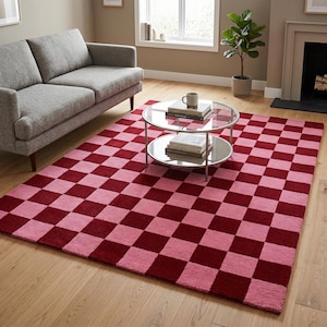 May include: A rectangular area rug featuring a repeating checkerboard pattern in alternating shades of deep burgundy red and soft pastel pink. The rug is constructed with a textured pile and covers a significant portion of the light wood floor.
