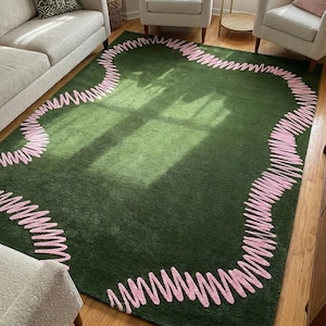 May include: A green rug with a pink, scribbled border. The rug is rectangular and covers a large area of the wooden floor. The pink border is a continuous line that follows the rug's edge, creating a unique design.