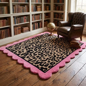 May include: A rectangular area rug featuring a central leopard print pattern in shades of tan, brown, and black, framed by a thick, solid pink scalloped border. The rug is laid flat on a wooden floor, showcasing its textured surface and edges.