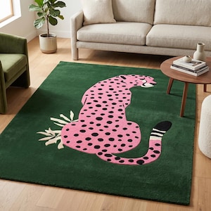Op de afbeelding: Een rechthoekig groen tapijt met een roze cheetah-ontwerp met zwarte stippen. De cheetah zit met zijn staart opgerold en witte bladeren bevinden zich in de buurt van zijn voorpoten. Het tapijt bevindt zich in een woonkamer.