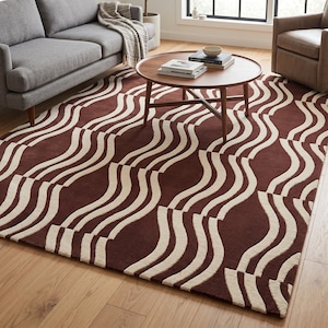 May include: A rectangular area rug with a repeating pattern of cream-colored, wavy lines on a deep burgundy background. The rug is placed on a hardwood floor, with a gray sofa and a wooden coffee table in the background.
