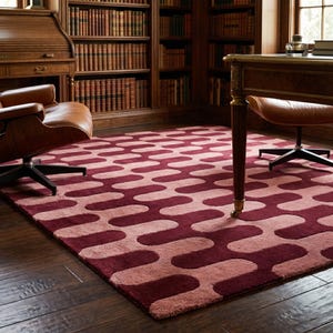 Puede incluir: Una alfombra rectangular con un patrón repetitivo de formas alargadas y redondeadas en tonos burdeos y rosa claro. La alfombra está colocada sobre un suelo de madera oscura en una habitación con una biblioteca y sillones de cuero.