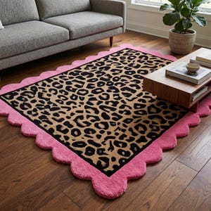 May include: A rectangular area rug featuring a central leopard print pattern in shades of tan, brown, and black. The rug is framed by a wide, solid pink scalloped border with a textured, tufted surface that extends around the entire perimeter.