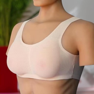 Puede incluir: Un sujetador deportivo de color beige claro con un diseño de tejido texturizado y microperforado. La prenda presenta un escote redondo amplio, tirantes gruesos y una construcción sin costuras que ofrece una silueta lisa y ajustada al pecho.
